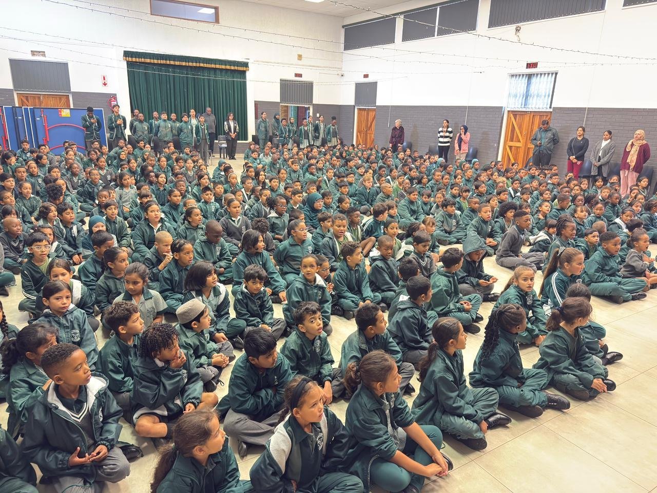 Large group of students in school uniforms sitting on gymnasium floor during assembly or gathering