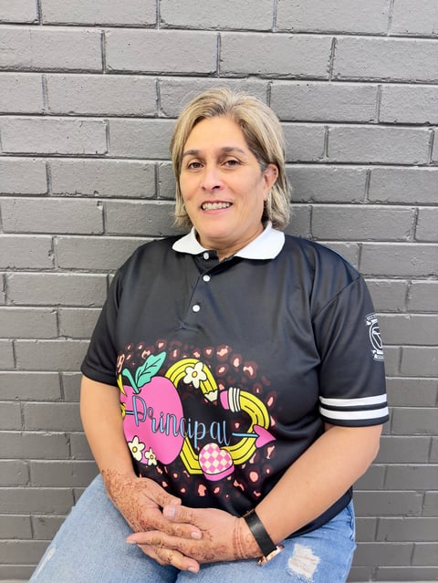 Person with blonde hair wearing a black polo shirt with colorful graphic design, smiling at camera against a gray brick wall
