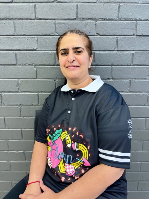 Woman smiling at camera wearing black polo shirt with colorful graphic design and white collar, standing in front of gray brick wall