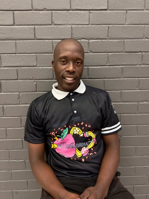Man smiling at camera wearing black polo shirt with colorful graphic design, posing against gray brick wall
