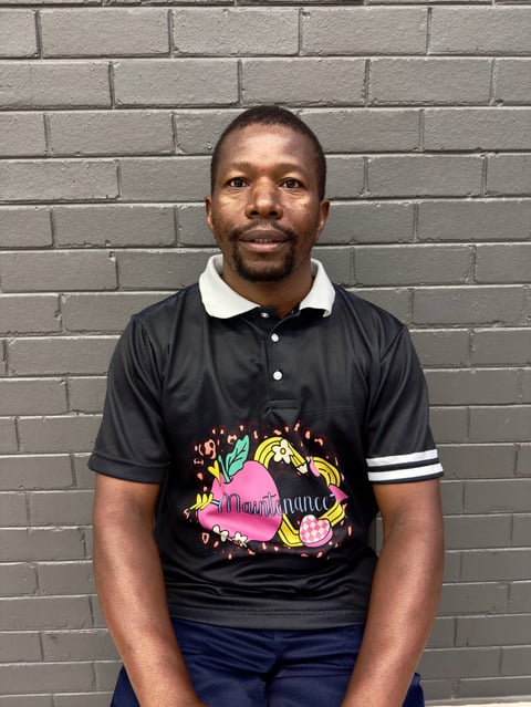 Portrait of a man wearing a black polo shirt with colorful graphic print and navy pants, standing against a gray brick wall