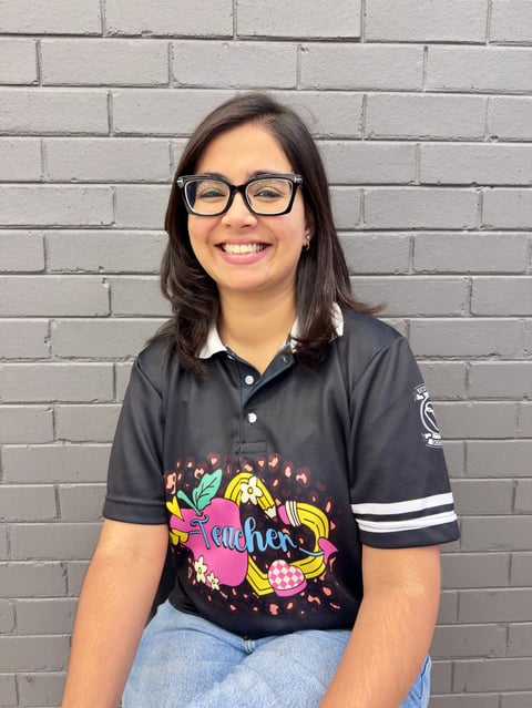 Smiling young woman wearing glasses and a colorful black polo shirt seated in front of a brick wall