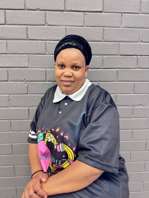 Portrait of a person wearing a navy polo shirt with graphic design, navy headband, and white collar, standing in front of a white brick wall