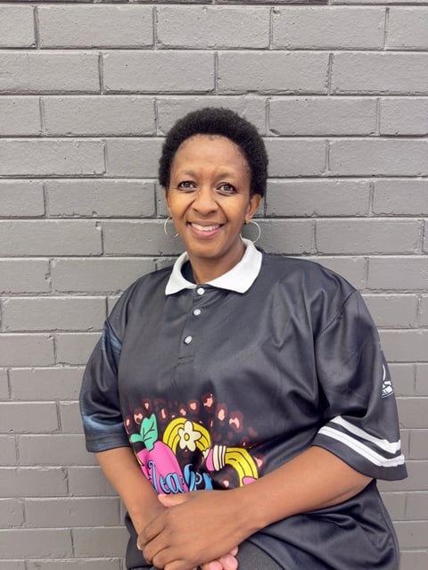 Woman smiling at camera wearing black polo shirt with colorful graphic print, standing against gray brick wall