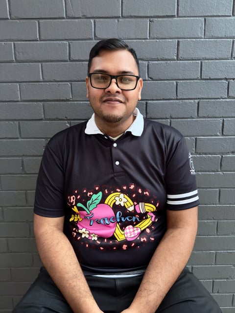 Man wearing black polo shirt with colorful graphic design sitting against gray brick wall