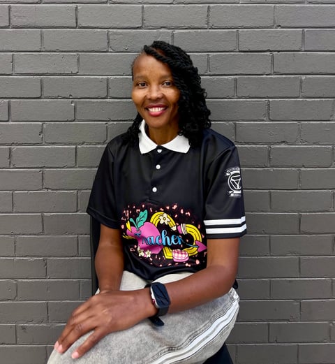 Portrait of a smiling woman with long dark hair wearing a black and white polo shirt with colorful graphic design, posing against a gray brick wall