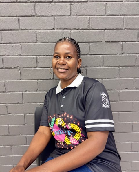 Woman smiling at camera wearing black polo shirt with colorful graphic design against gray brick wall