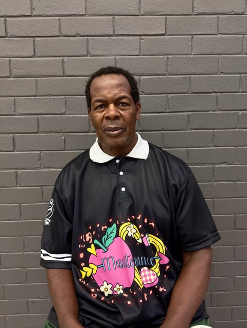 Middle-aged man wearing black polo shirt with colorful graphic design, standing against gray brick wall