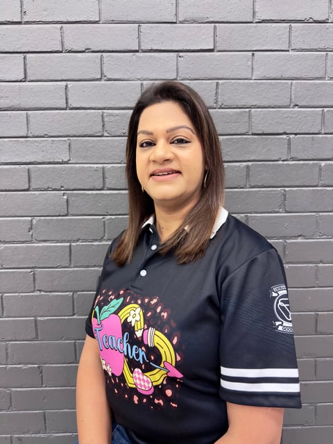 Woman with long dark hair wearing a black polo shirt with colorful graphic design, standing against a gray brick wall